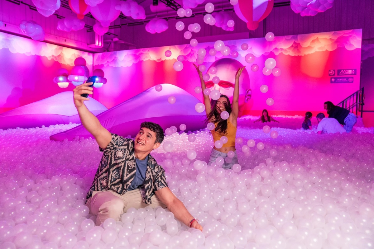 People having fun in a colorful ball pit, taking selfies and playing with white plastic balls at Bubble Planet