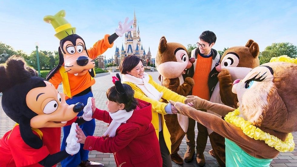 People high-fiving Disney characters in front of a castle at a Tokyo Disneyland