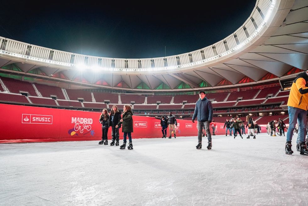 People ice skating inside a brightly lit stadium at night in Madrid.
