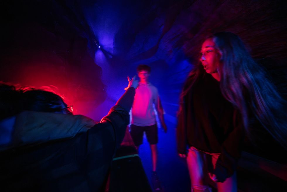 People in a dim, colorful tunnel with vibrant red and blue lighting.