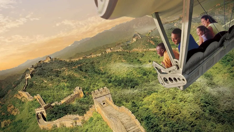 People in a flight simulator soar over the Great Wall of China at sunset.