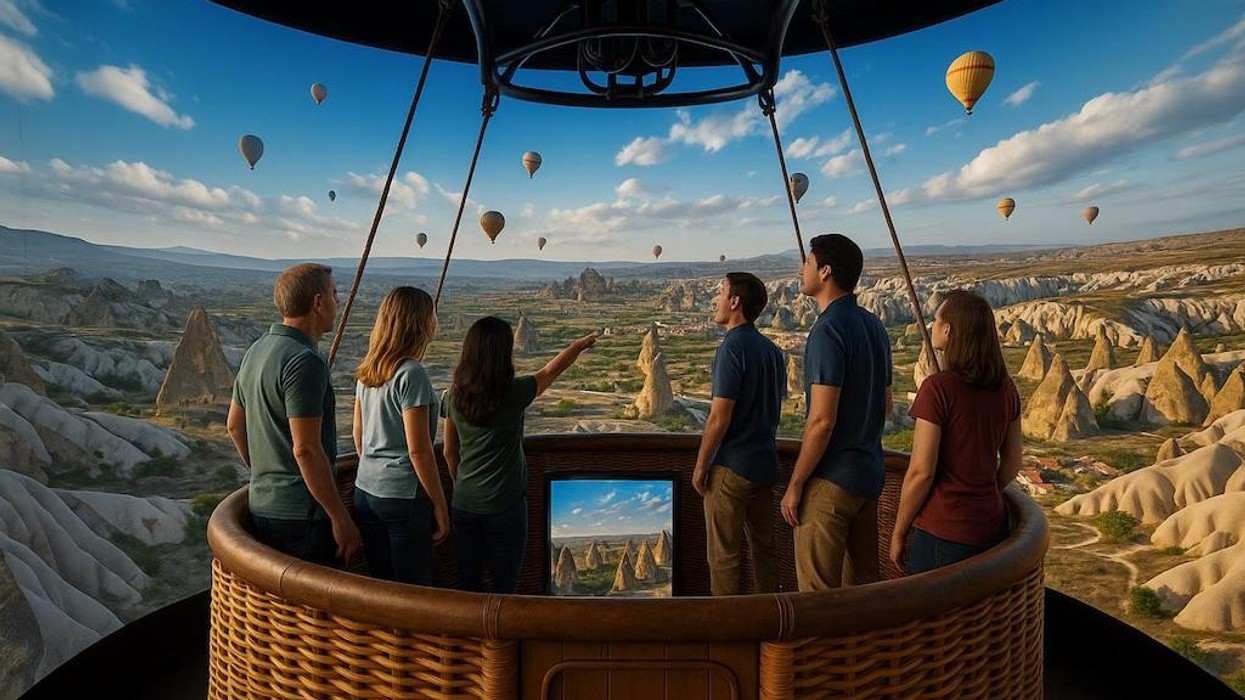 People in a hot air balloon admire a landscape with rock formations and other balloons.