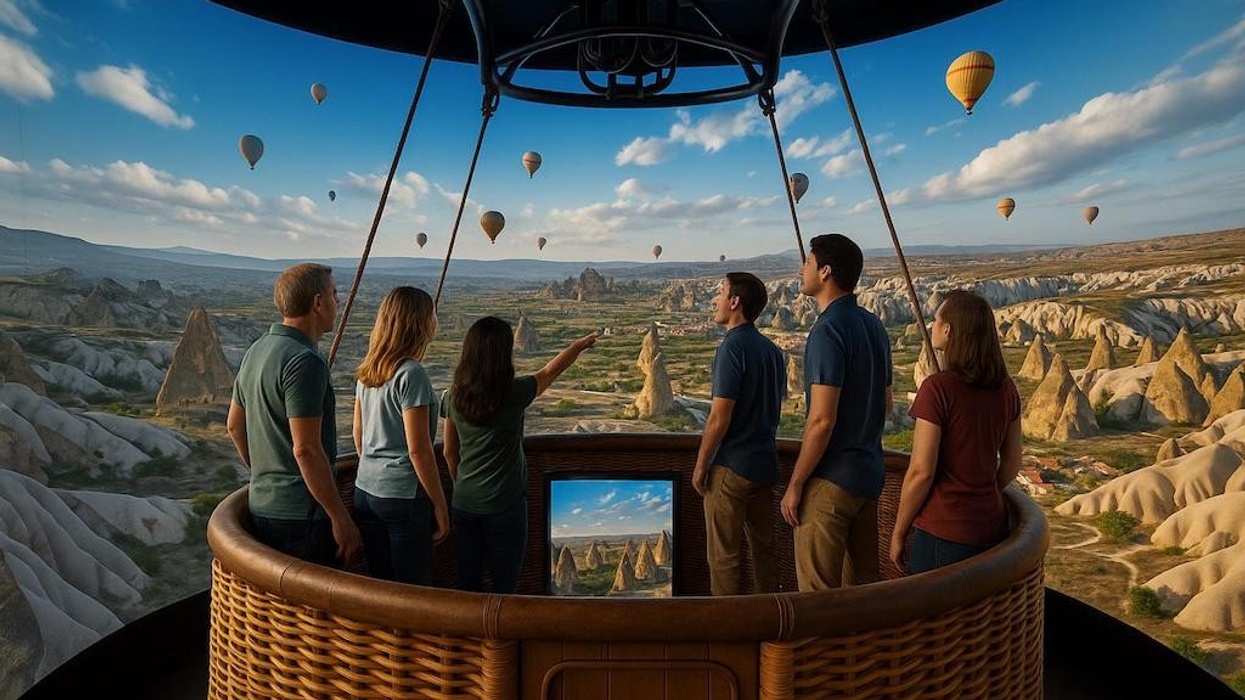 People in a hot air balloon admire a landscape with rock formations and other balloons.