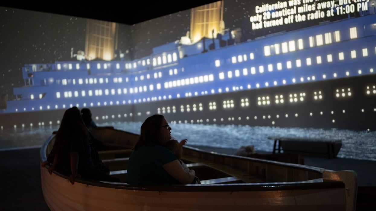 People in a lifeboat viewing a projected ship at the exhibition, Titanic: An Immersive Voyage.