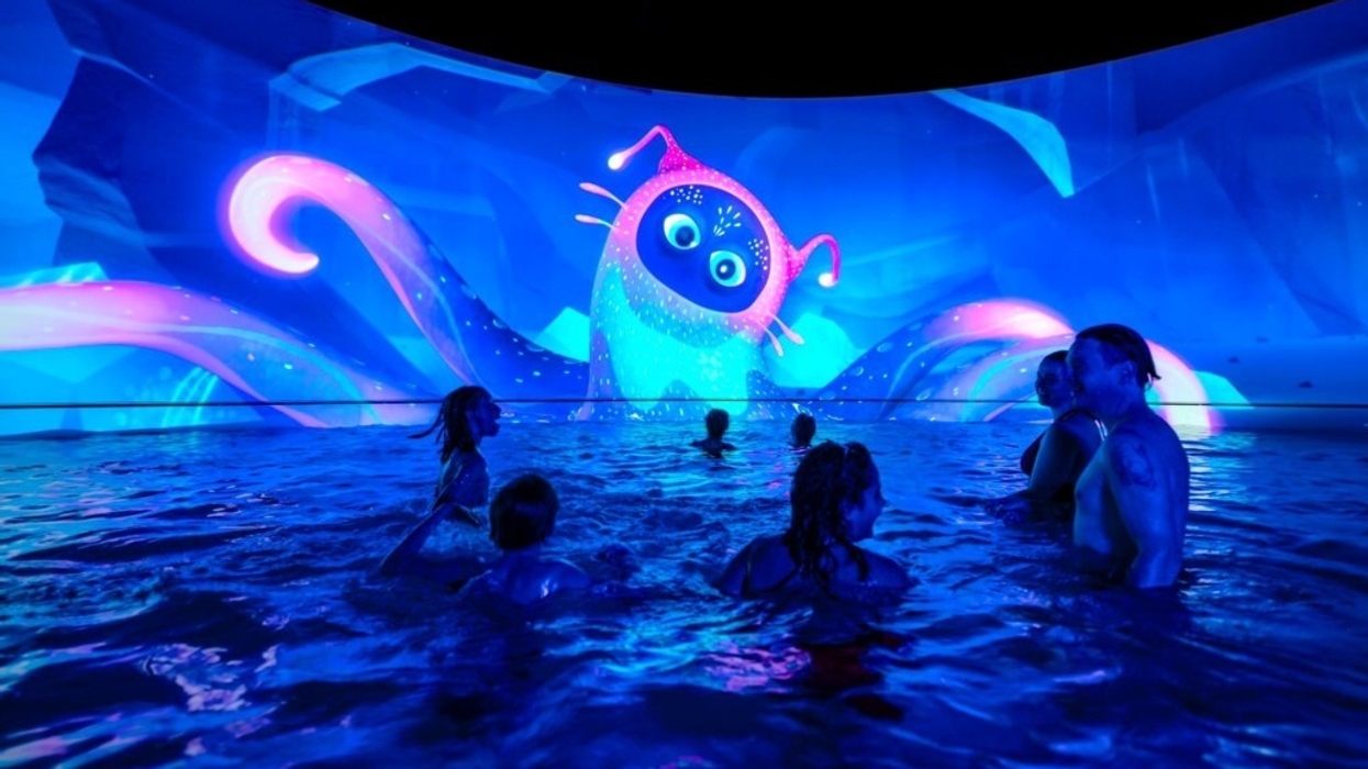 People in a pool at Aquascope in France, watching a bright, animated creature on a large screen.