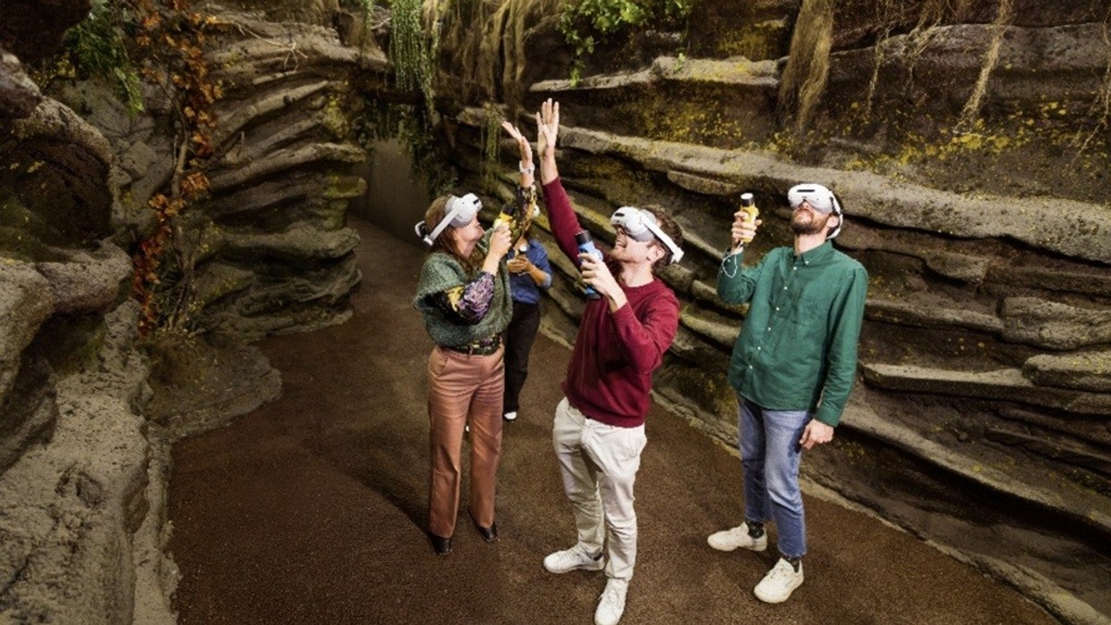 People in a rocky cave wearing VR headsets, holding controllers, looking up.