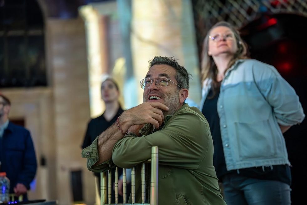 People in a room, one man smiling thoughtfully, observing something above.