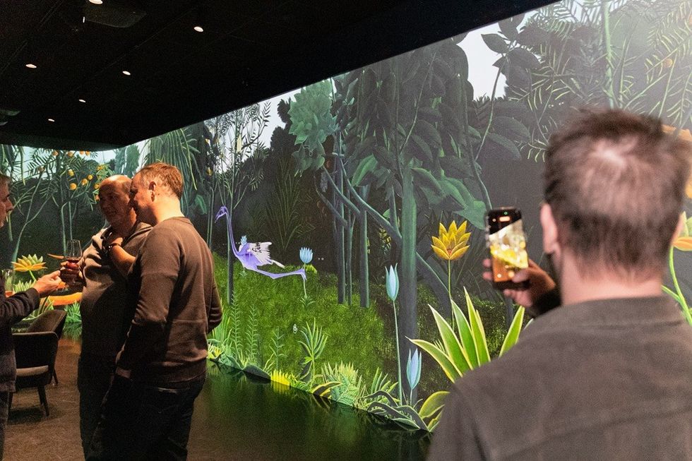 People in a room with a vibrant jungle projection, one taking a photo.