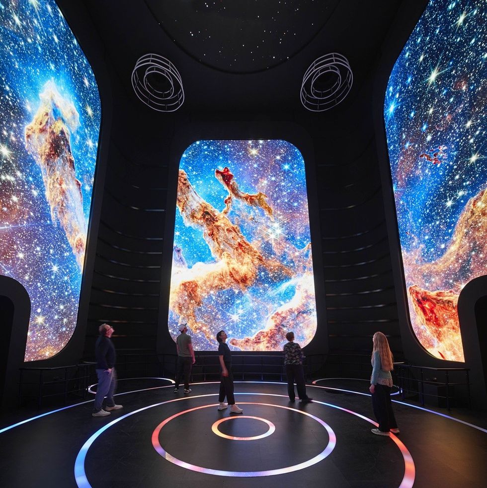 People in a room with large screens displaying vibrant space scenes.
