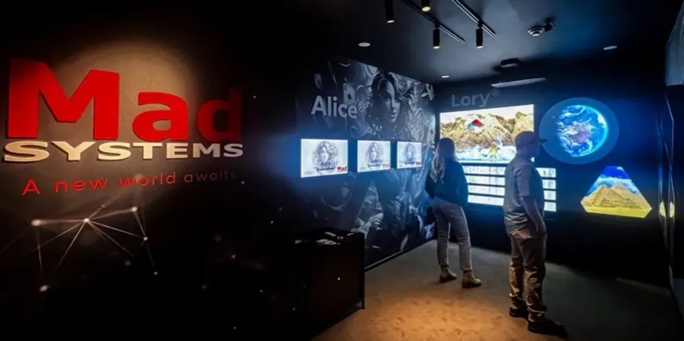 People in a tech exhibit room with interactive screens and "Mad Systems" signage.