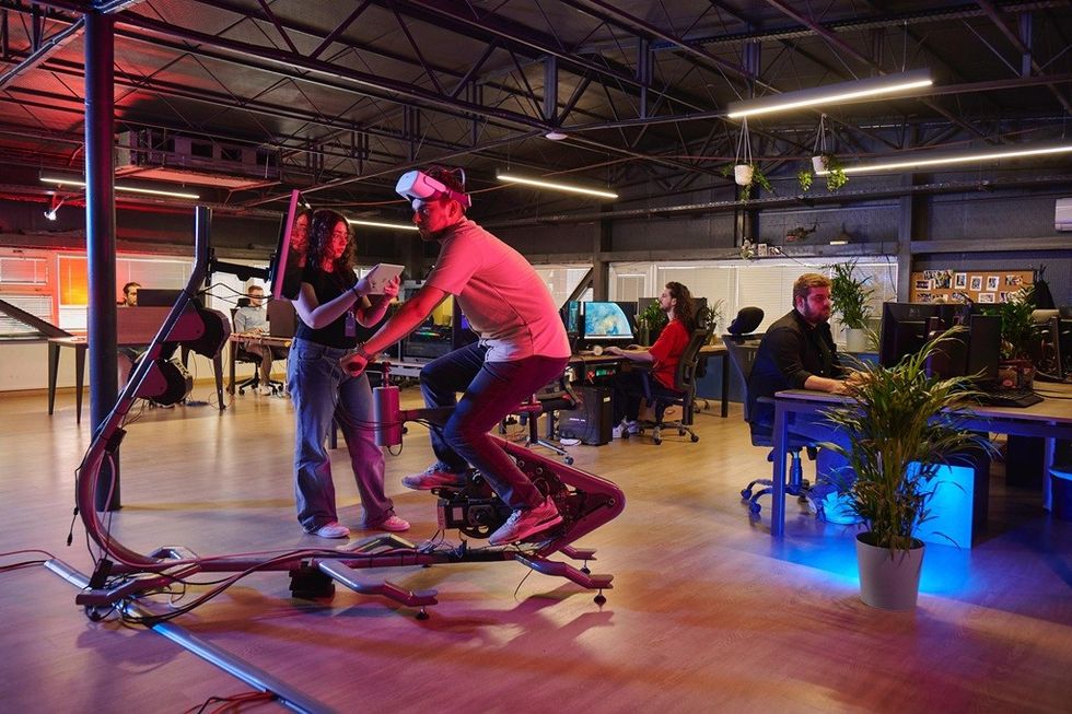 People in a tech office, one using a VR headset on a stationary bike.