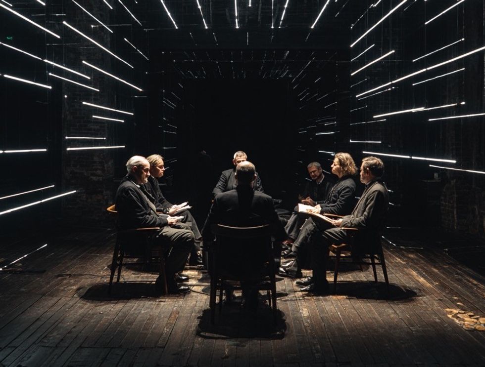 People in dark room seated in a circle, surrounded by lines of light.
