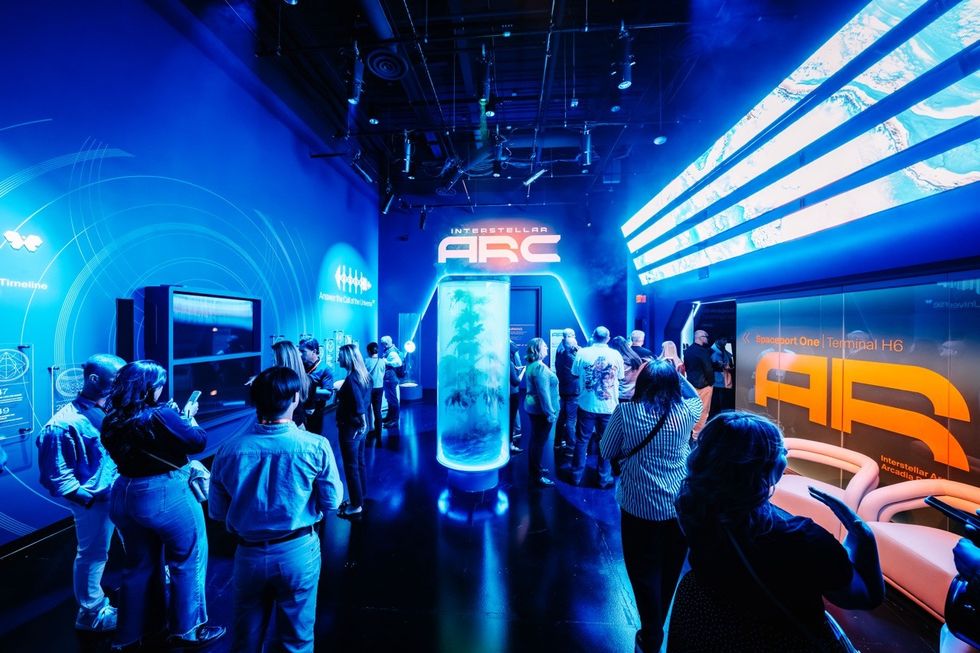 People in futuristic exhibit space with blue lighting and "Interstellar ARC" signage.