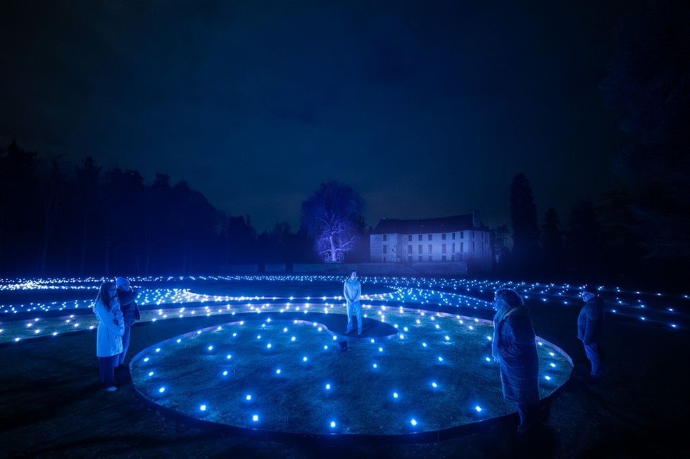 People in illuminated blue circle with lights, large house and trees in the background at night.