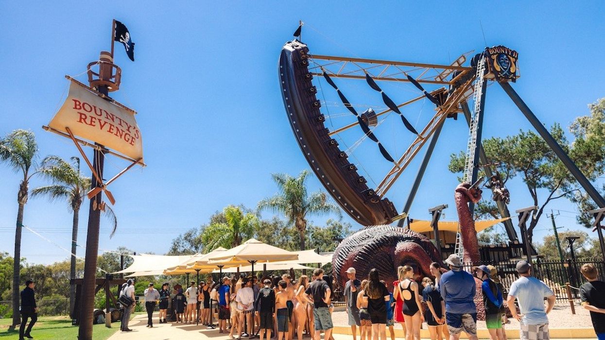 People in line at "Bounty's Revenge" pirate ship ride, sunny day, palm trees around.