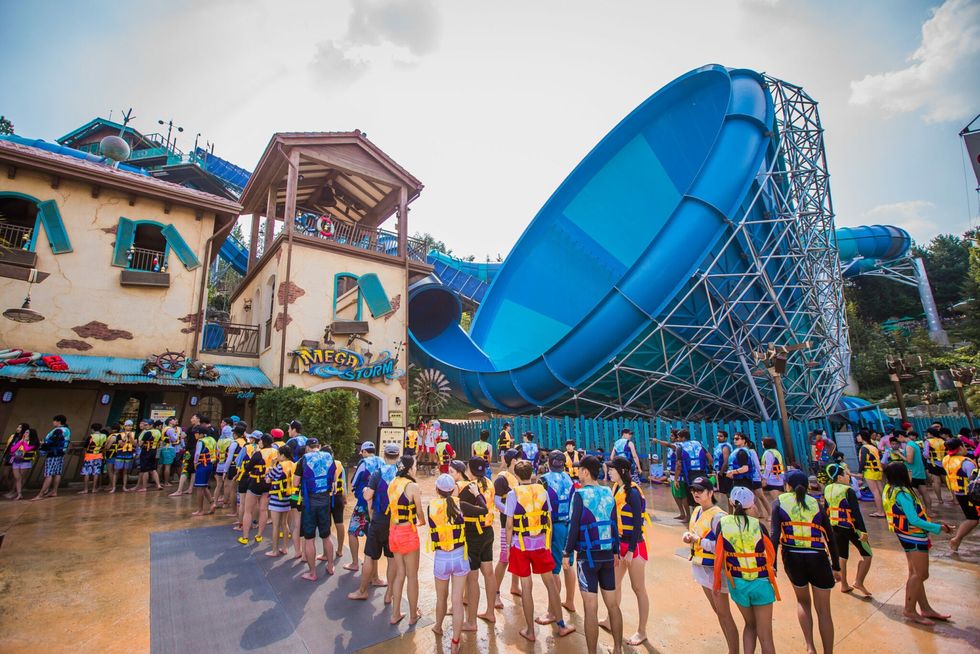 People in line at Caribbean Bay water park, wearing life jackets near a large blue slide.