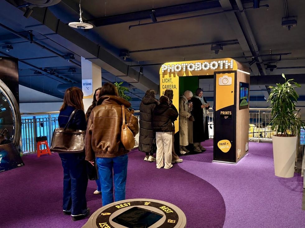 People in line for a photobooth on a purple carpet in a modern building.