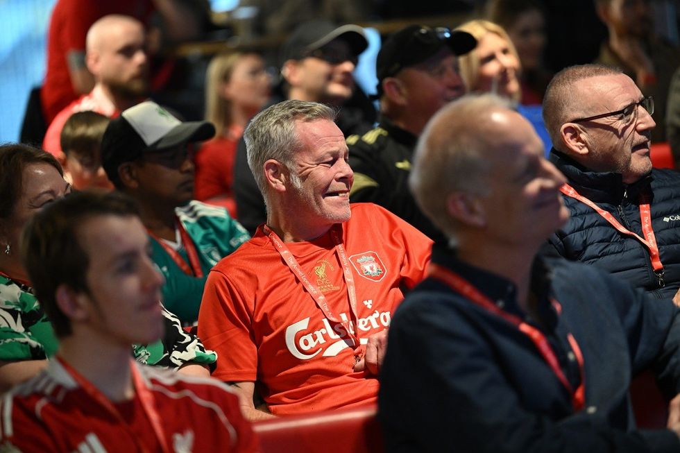People in Liverpool football shirts watching an event, smiling and engaged.