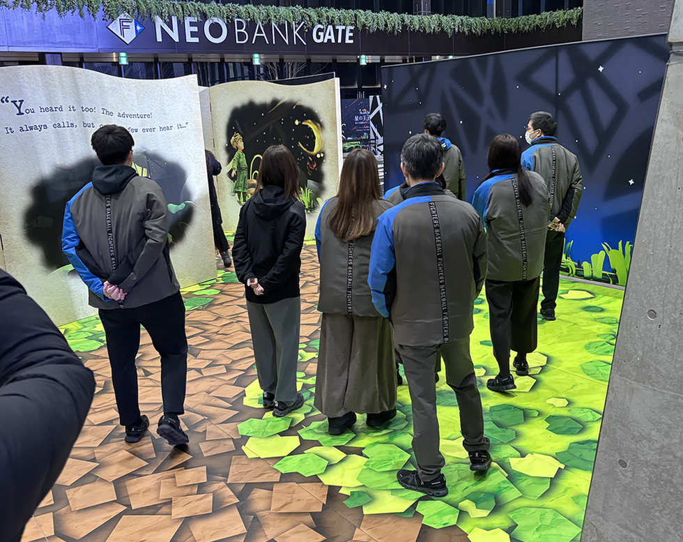 People in matching jackets looking at a large storybook display in a decorated room.
