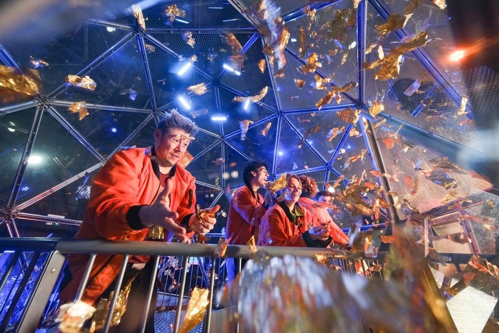 People in red jackets in glass dome with gold confetti swirling around.