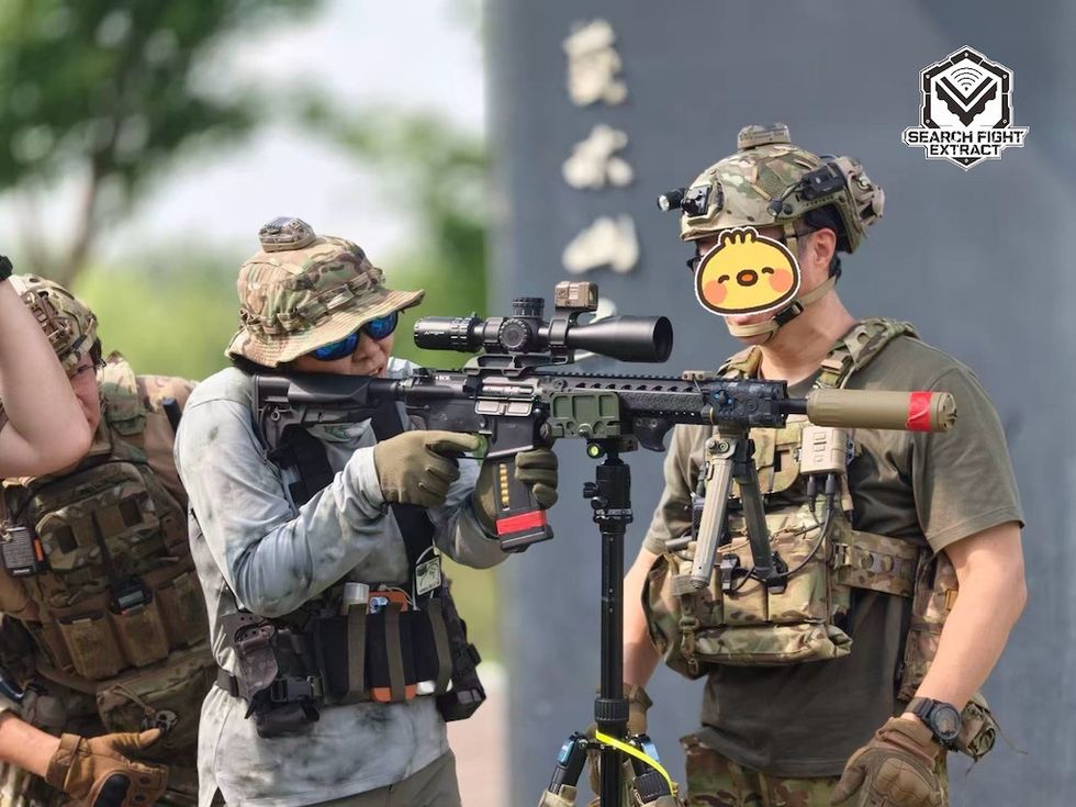 People in tactical gear using a scoped rifle on a tripod outdoors at Beijing Wenyu River Park