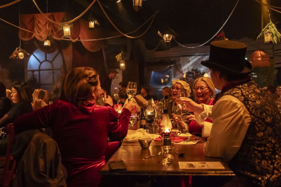 People in vintage attire enjoying a festive dinner in a warmly lit, decorated room.