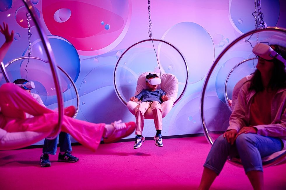 People in VR headsets on bubble chairs in a vibrant, colorful room.