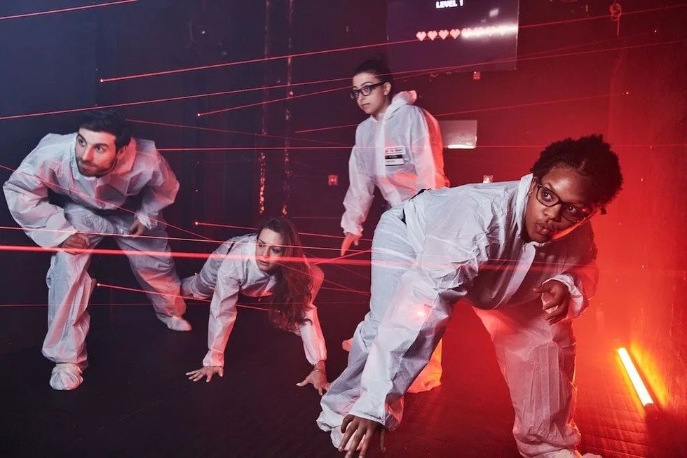 People in white suits navigate a room with red laser beams at Beat the Bomb
