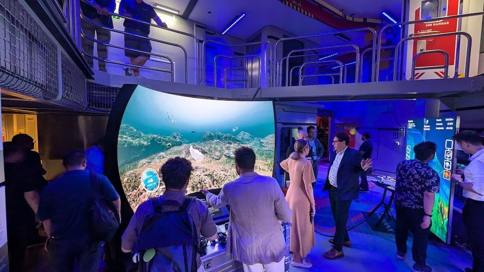 People interact in a futuristic room with large screens and blue ambient lighting.