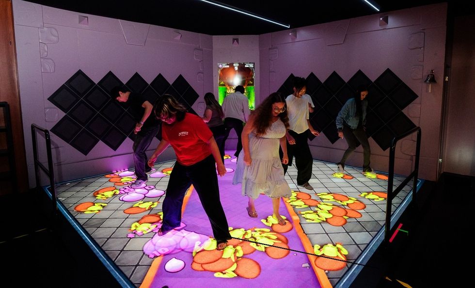 People interact on a colorful, floor-projected game platform indoors.