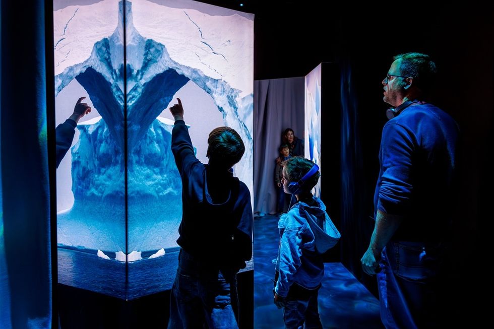 People interact with a large, illuminated iceberg display in a dark room at \u200bPolar Experience.