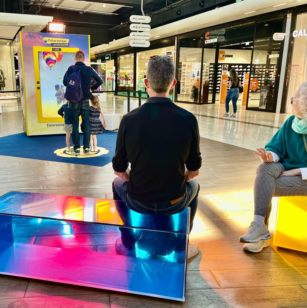 People interact with a mirrored booth in a bright shopping mall setting.