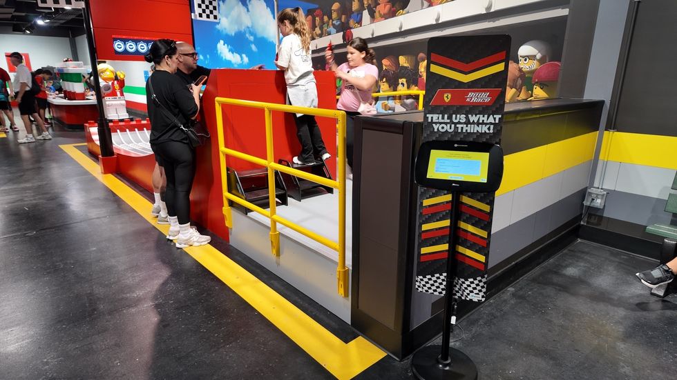 People interacting in a LEGO-themed indoor play area with a feedback kiosk.