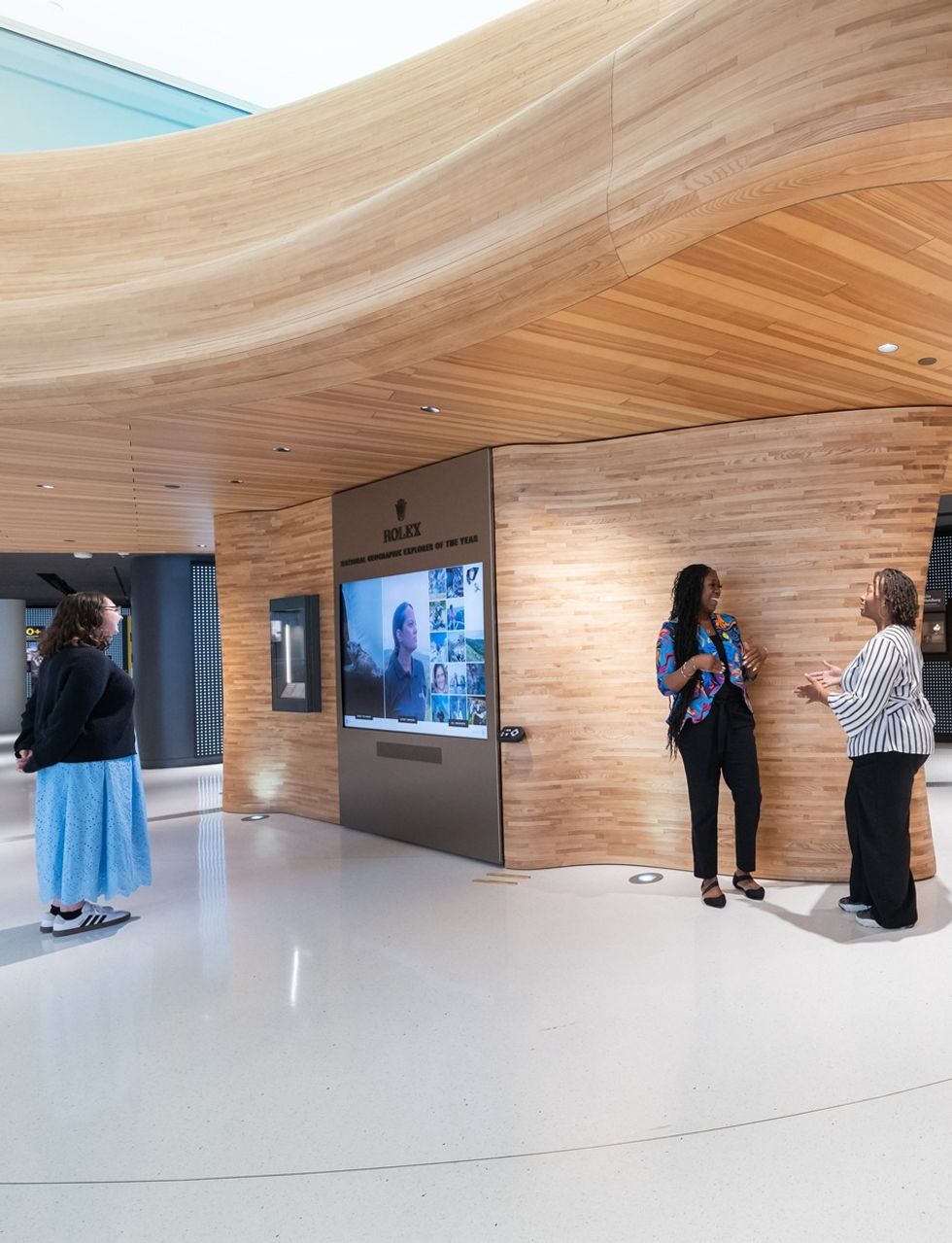 People interacting in a modern, wooden-paneled exhibit space with a digital display at the National Geographic Museum of Exploration