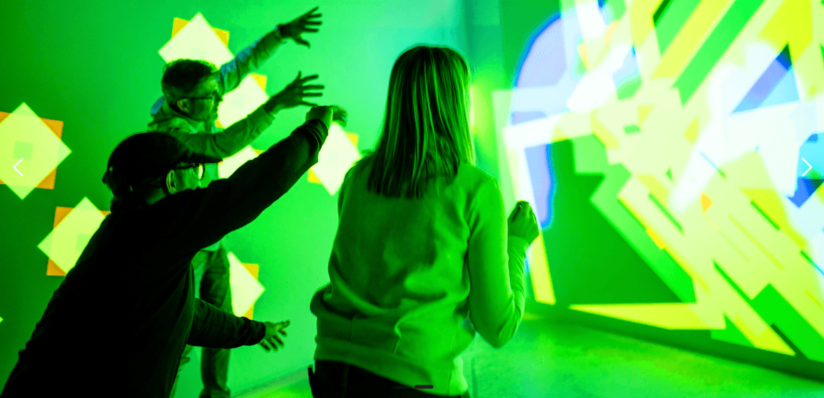 People interacting with a bright green and yellow geometric light display at Electric Playhouse Travels