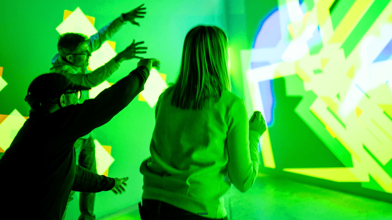 People interacting with a bright green and yellow geometric light display at Electric Playhouse Travels