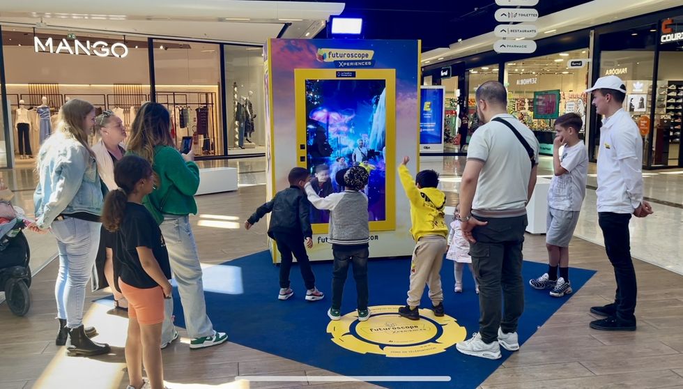 People interacting with a colorful digital kiosk in a bustling shopping mall.