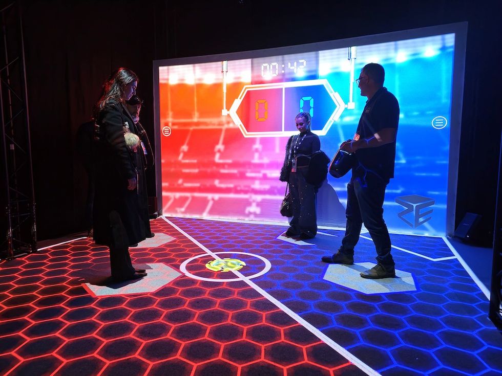 People interacting with a red and blue digital game floor, large screen in the background.