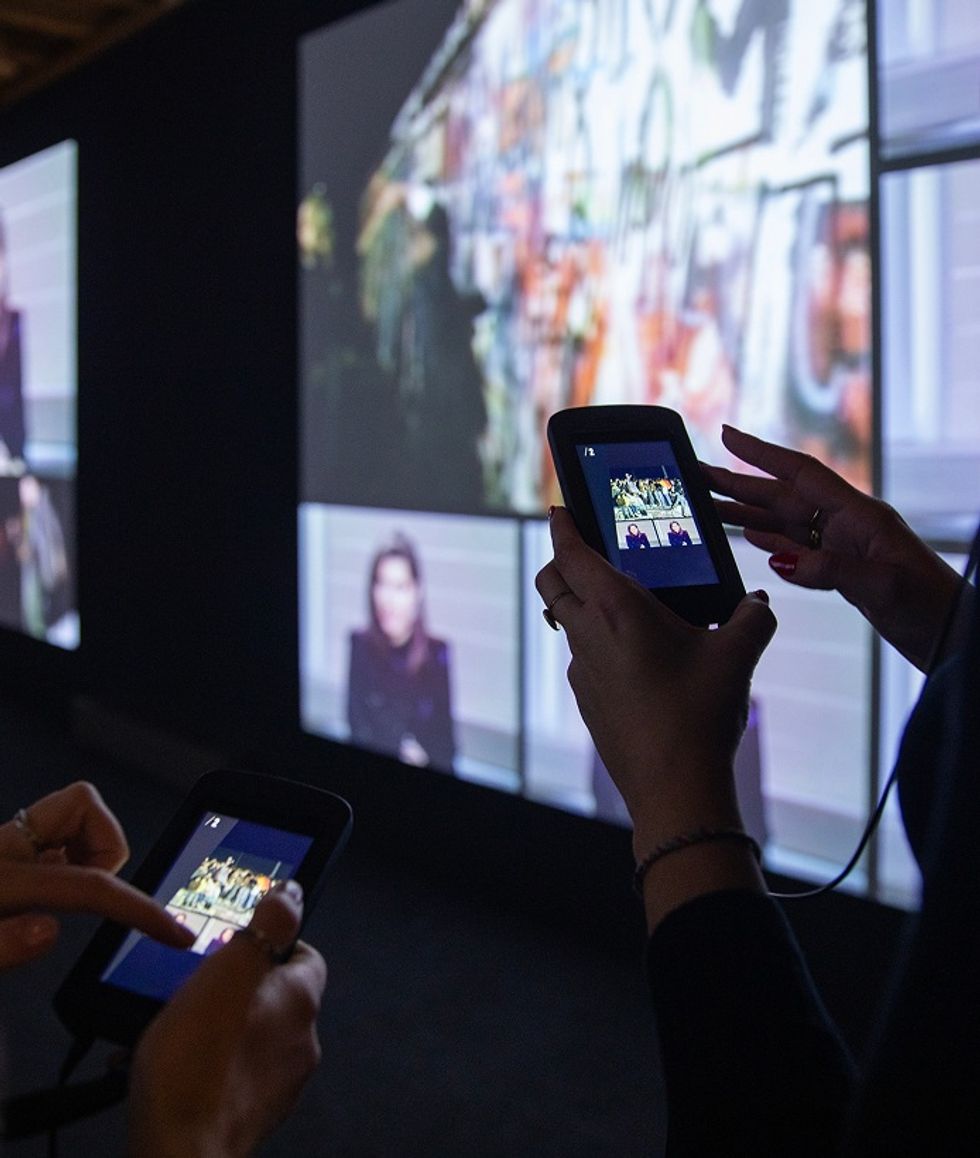People interacting with digital devices in front of a large, colorful screen display.
