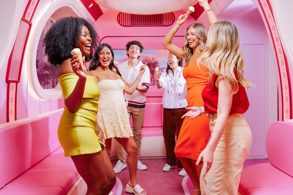 People joyfully dancing in a pink-themed room holding ice cream cones.