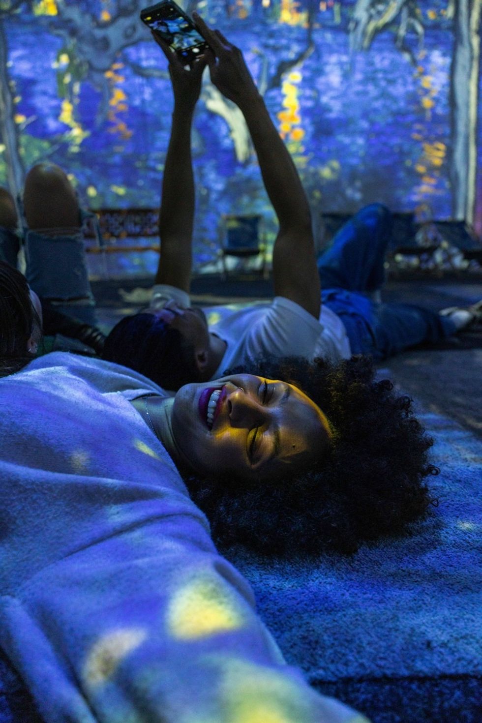 People lie on a floor with vibrant, colorful lights and a projected background at Van Gogh: The Immersive Experience in Cincinnati, US.