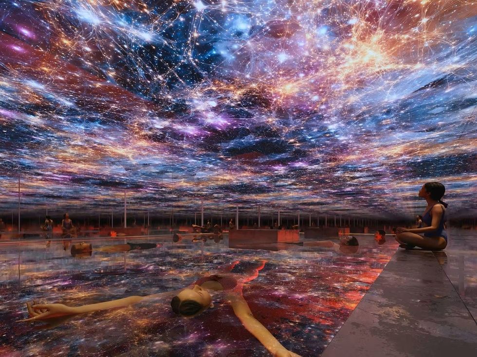 People lounge by a reflective pool under a vibrant, starry sky projection.