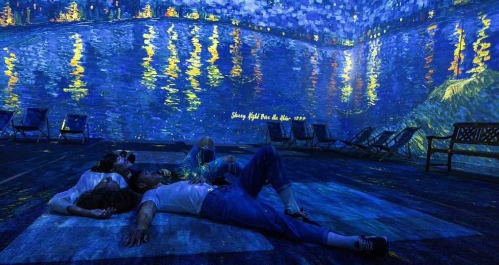 People lying on the floor under a Van Gogh art projection, creating a tranquil atmosphere.