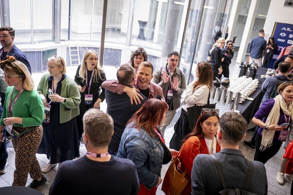 People mingling and chatting at a conference with coffee table setup in the background.