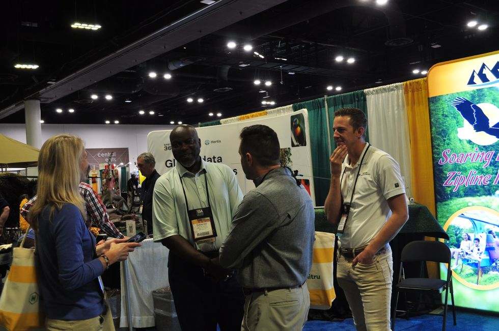 People networking at an indoor exhibition booth with signage and displays.