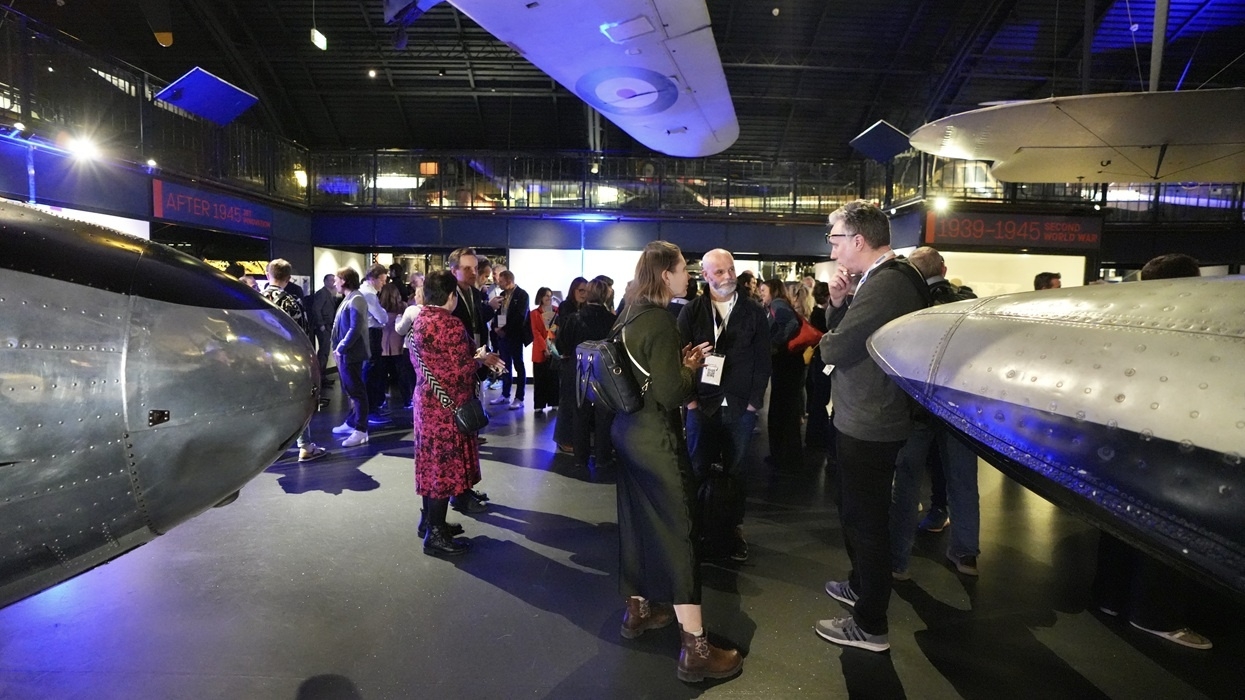 People networking at the InnovateX conference, in an aviation museum surrounded by aircraft exhibits.