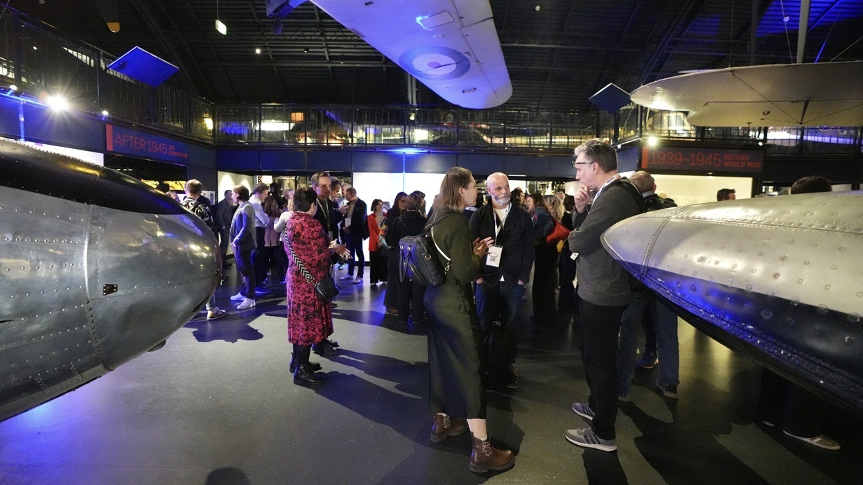 People networking at the InnovateX conference, in an aviation museum surrounded by aircraft exhibits.