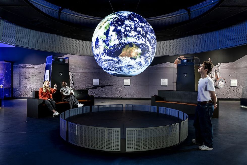 People observe a large Earth model inside a modern space-themed exhibit.