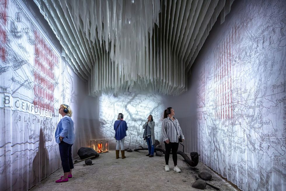 People observe a map projection in a room with a textured ceiling and ambient lighting. The War Rooms at The Story of Emily