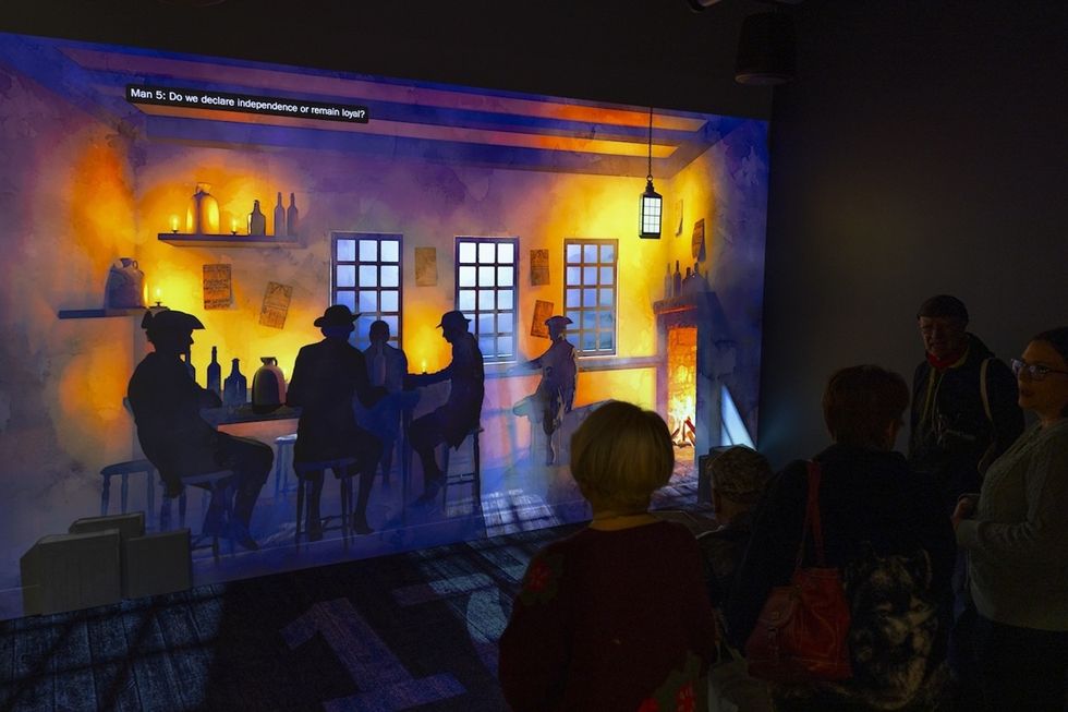 People observing a historical scene projection in a dimly lit room.